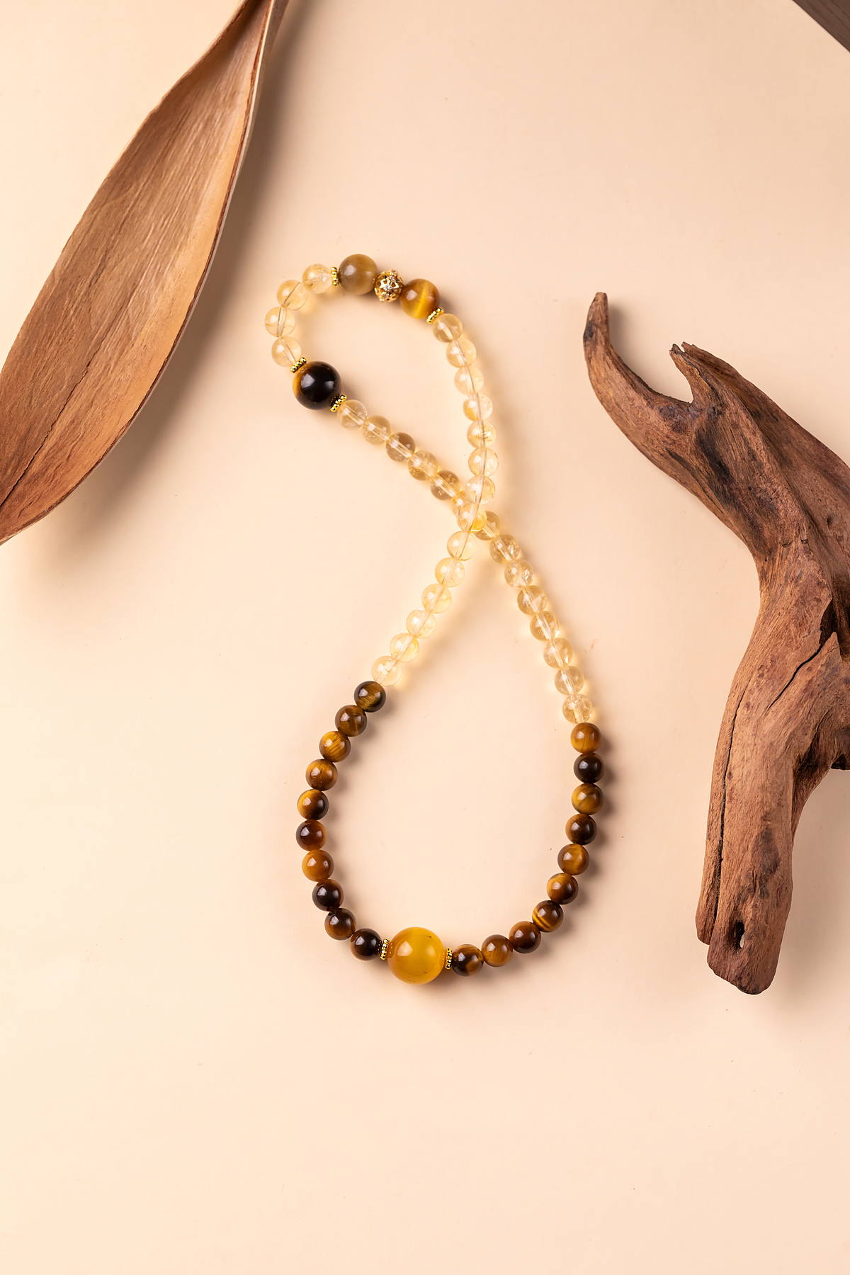A long strand of citrine, tiger's eye and yellow jade beads laid in a figure eight beside driftwood.